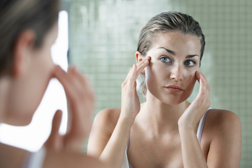 Woman applying skin cream in front of mirror